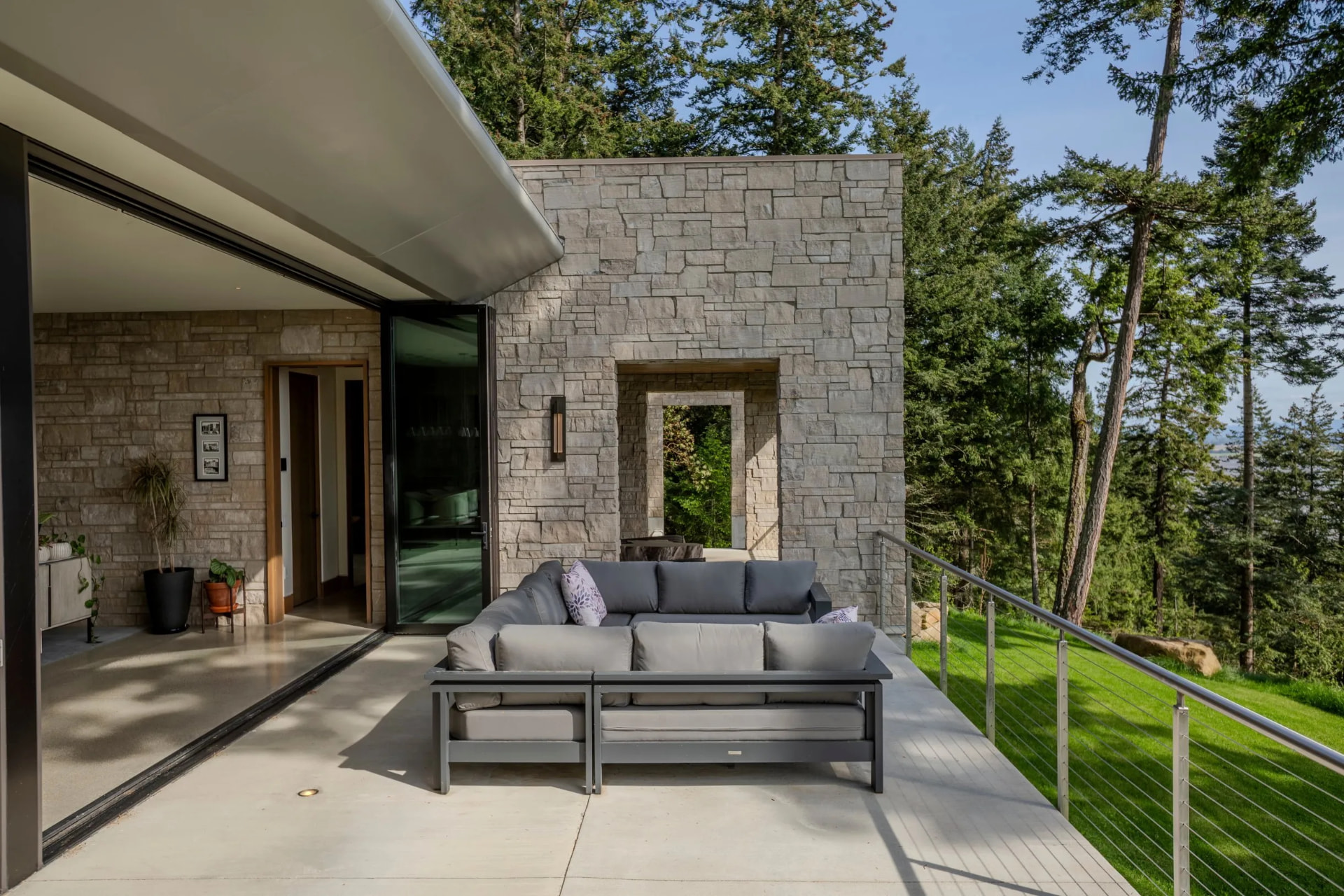 Modern cut-stone veneer walls framing a covered terrace above evergreens