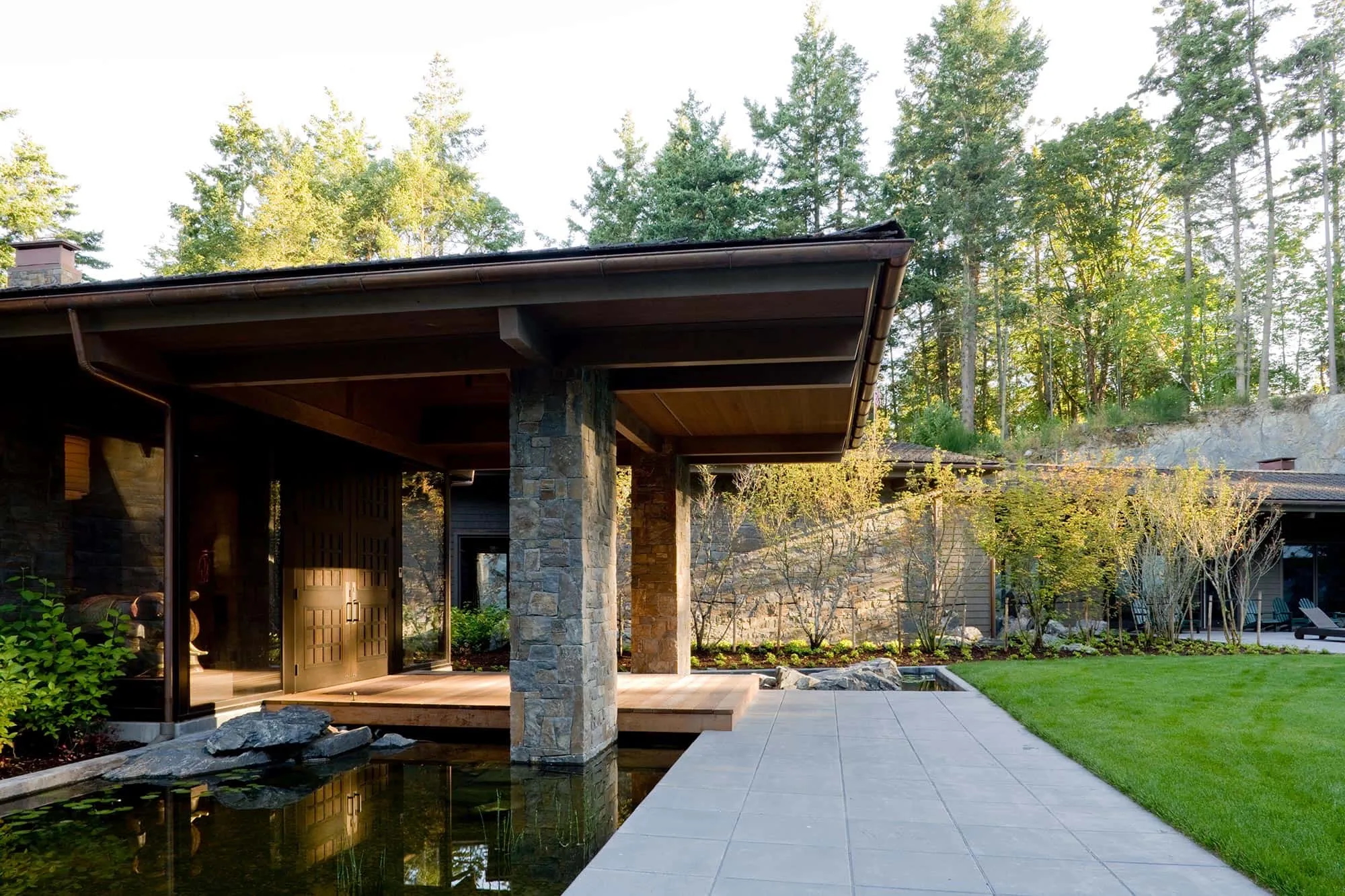 Stone columns and dry-stack wall beside a reflecting pool and entry deck