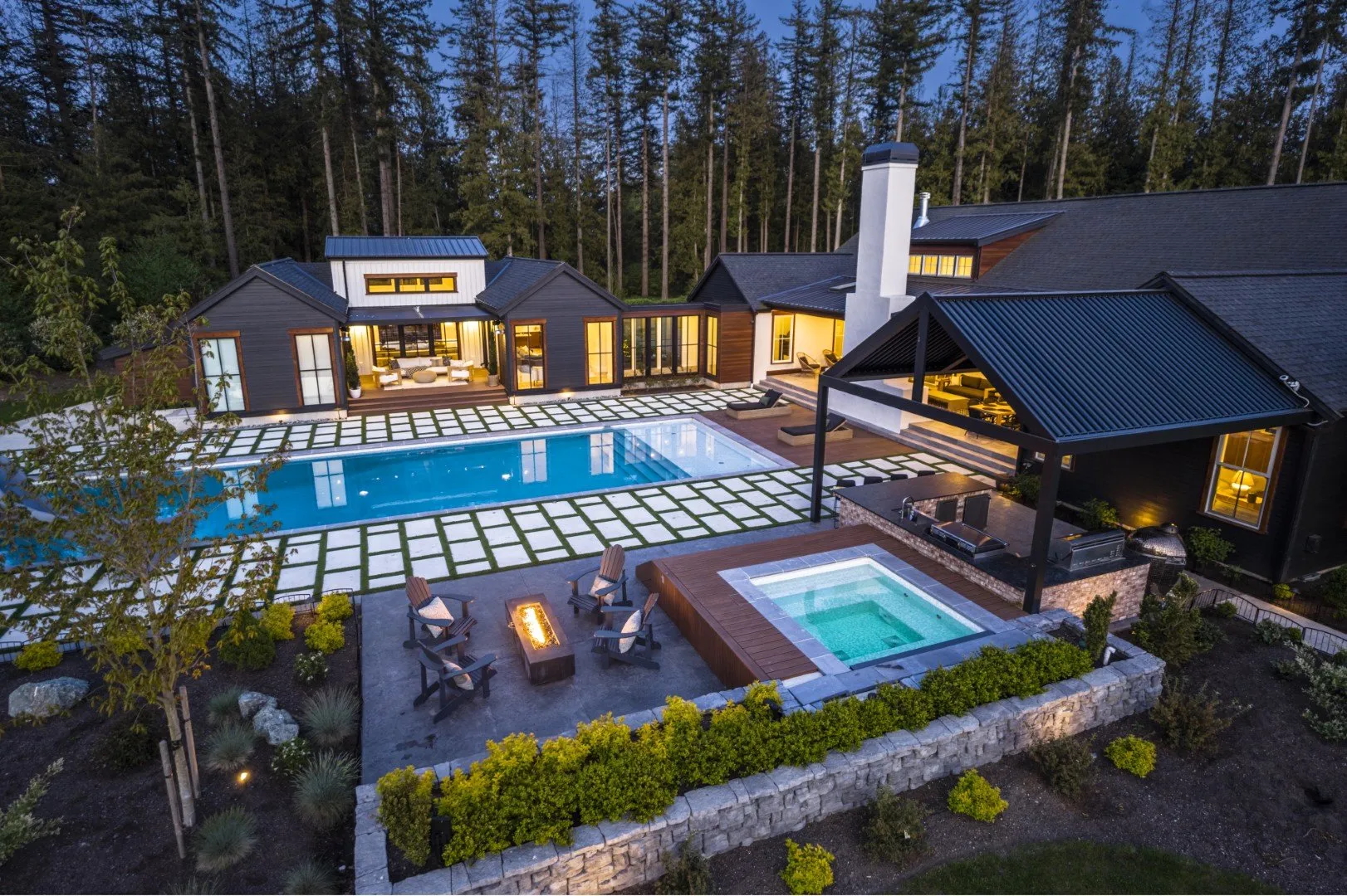 Poolside masonry with stone seat walls, outdoor kitchen, and chimney at dusk